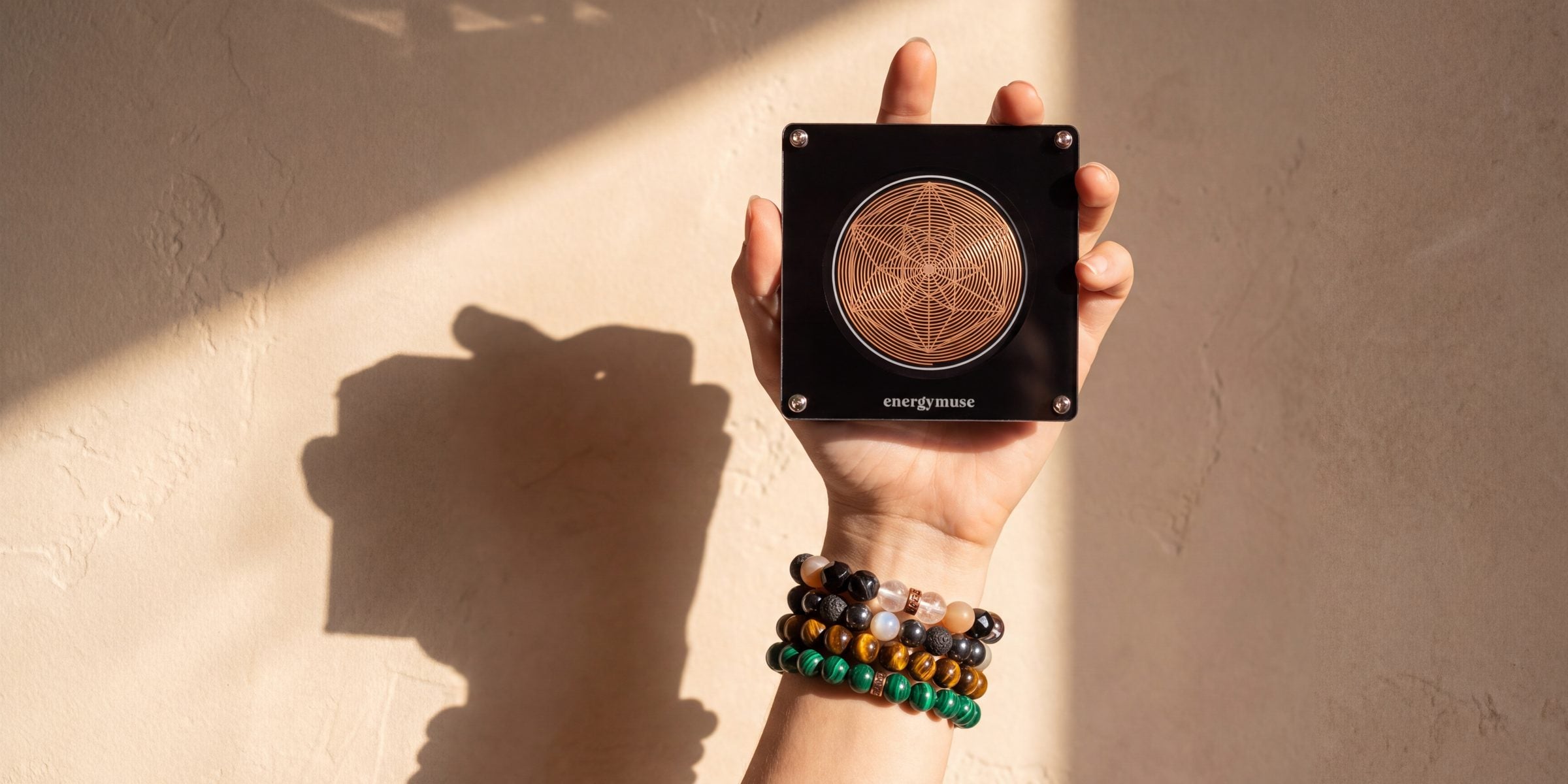 A raised hand wearing beaded gemstone bracelets beside a copper-charged crystal, lit by warm afternoon sun